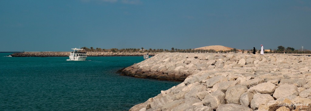 Sur la jetée face à Lulu Island, île qu'on recouvre de jardins et de palmiers, un homme et une femme marchent. L'homme est en blanc et la femme en noir, selon la tradition émirienne.